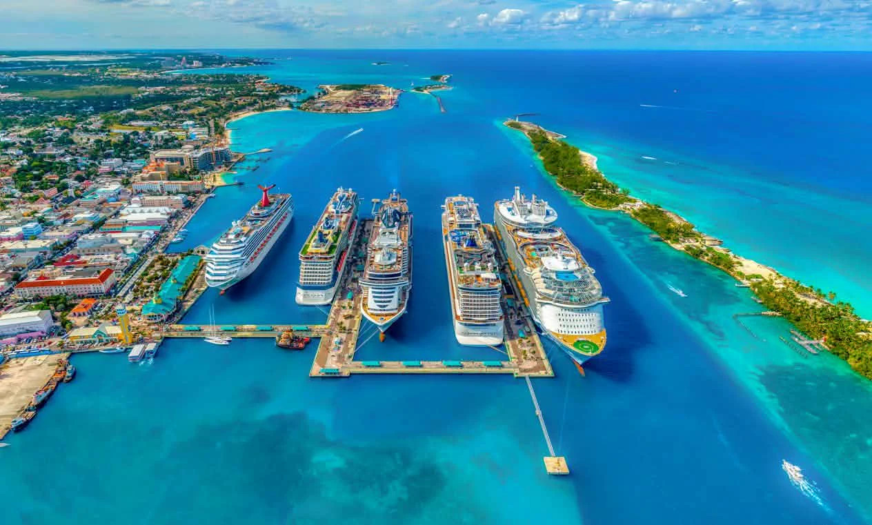 An aerial view of five cruise ships docked at a Bahamas port, surrounded by turquoise ocean water